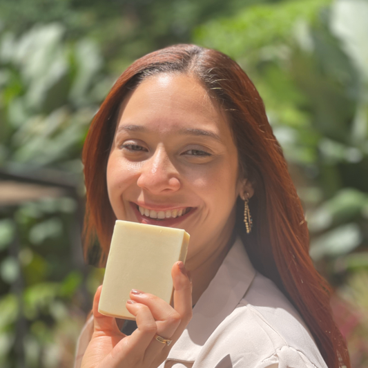 Woman holding a natural mild bar of soap outdoors with greenery in the background
