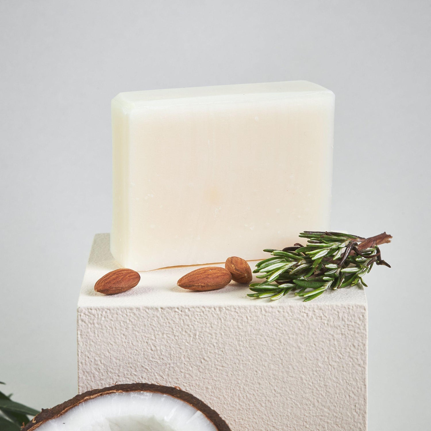 Bonuderm Rosemary Bar Soap next to raw rosemary sprigs, almonds, and coconut pieces.