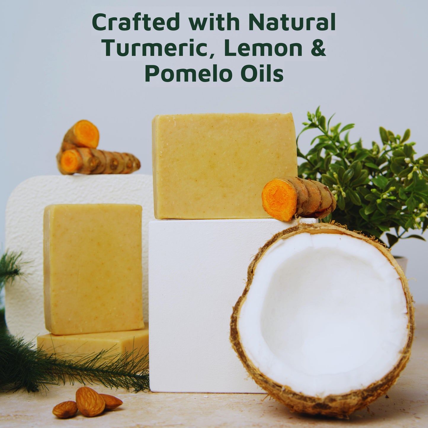Three real turmeric soaps on a white stand with turmeric, lemon, and pomelo fruits, and a coconut, against a light gray background.